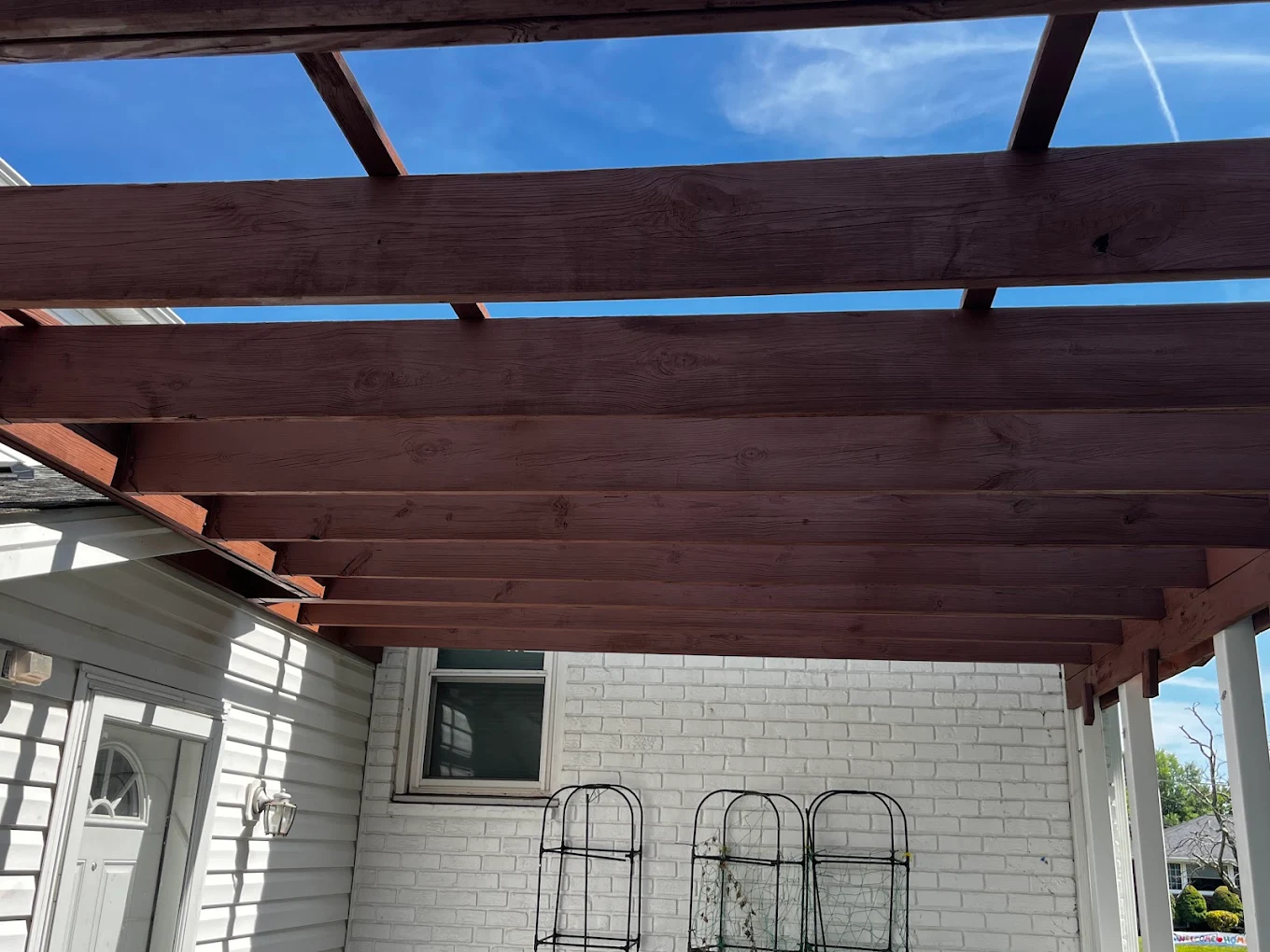 Pergola beams re-stained a deep mahogany above a white brick patio wall